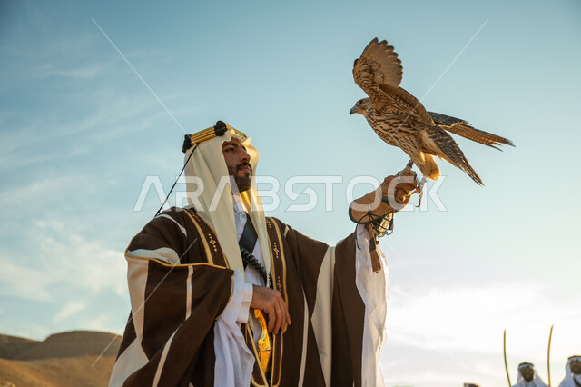 العناية بتربية الطيور و تدريبها, مكانة الصقور في التاريخ السعودي, صورة مقربة لرجل عربي خليجي سعودي يرتدي الغترة والبشت يحمل على يده طائر الصقر بتعابير الفخر, يوم بدينا 22 فبراير، ذكرى تاسيس الدوله السعوديه الاولى 1727 م, مناسبة وطنيه شعبيه