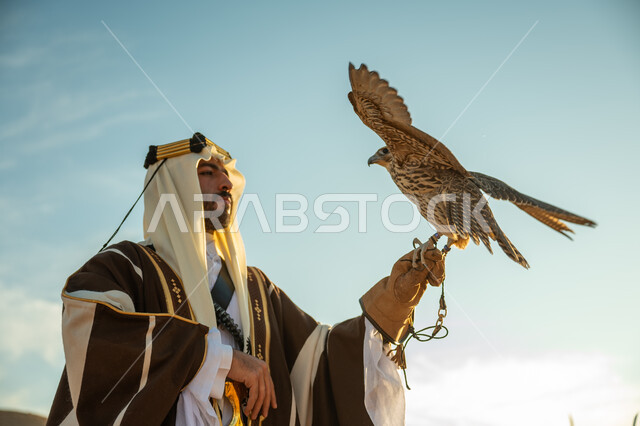 الاهتمام بتربية الطيور و تدريبها, مكانة الصقور في التاريخ السعودي, صورة مقربة لرجل عربي خليجي سعودي يرتدي الغترة والبشت يحمل على يده طائر الصقر بتعابير الفخر, يوم بدينا 22 فبراير، ذكرى تاسيس الدوله السعوديه الاولى 1727 م, مناسبة وطنيه شعبيه