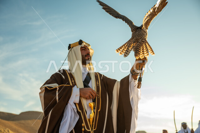 مناسبة وطنيه شعبيه, ذكرى تاسيس الدوله السعوديه الاولى 1727 م, يوم بدينا 22 فبراير، الاهتمام بتربية الطيور و تدريبها, مكانة الصقور في التاريخ السعودي, صورة مقربة لرجل عربي خليجي سعودي يرتدي الغترة والبشت يحمل على يده طائر الصقر, خلفية العرضة النجدية في الصحراء