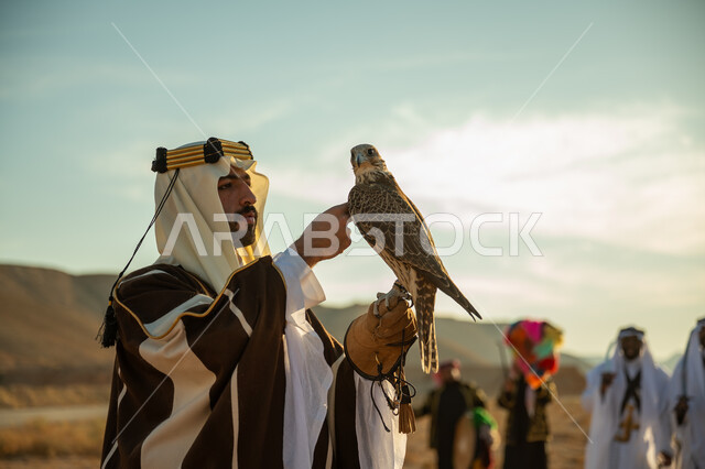 الاهتمام بتربية الطيور و تدريبها, مكانة الصقور في التاريخ السعودي, صورة مقربة لرجل عربي خليجي سعودي يرتدي الغترة والبشت يحمل على يده طائر الصقر, يوم بدينا 22 فبراير، ذكرى تاسيس الدوله السعوديه الاولى 1727 م, مناسبة وطنيه شعبيه, خلفية العرضة النجدية في الصحراء