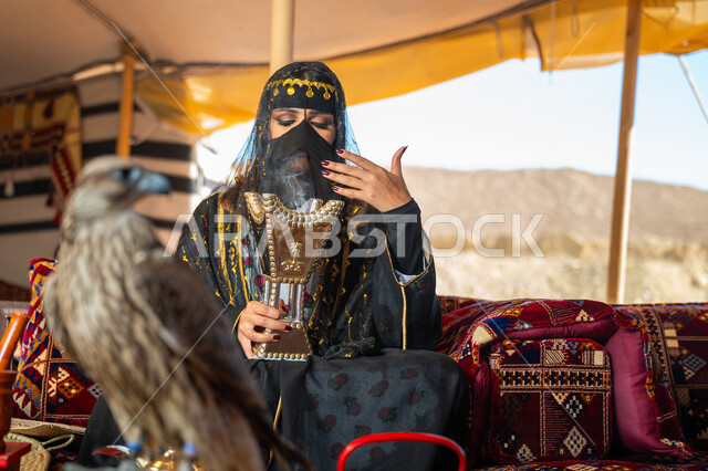 يوم بدينا 22 فبراير، الافتراس وحدة البصر, اتباع عادات وتقاليد دول الخليج بالتبخر، مكانة الصقور في التاريخ السعودي, ذكرى تأسيس الدوله السعوديه الأولى 1727م, امرأة عربية خليجية سعودية ترتدي الزي الشعبي للأعياد الوطنية والبرقع تحمل بيدها المبخرة وأمامها الصقر