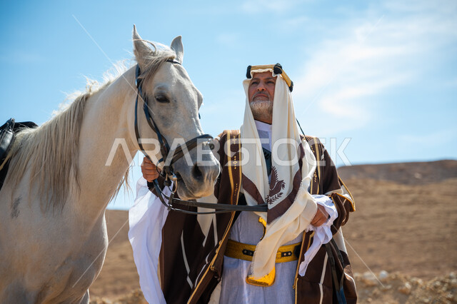 توراث حب وتربية الجياد من الأجداد, رعاية الخيل والاهتمام به في الصحراء، رجل عربي خليجي سعودي يرتدي العقال الذهبي والبشت يقف بجانب فرسه الأبيض الأصيل, ارتداء الزي الشعبي في المناسبة الوطنية، ذكرى تأسيس الدولة السعودية الأولى في 1727م, يوم بدينا  22 فبراير