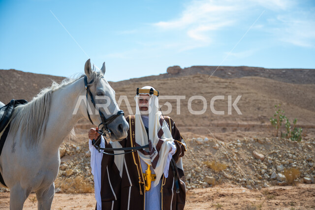 ذكرى تأسيس الدولة السعودية الأولى في 1727م, توراث حب وتربية الجياد من الأجداد, رعاية الخيل والاهتمام به في الصحراء، رجل عربي خليجي سعودي يرتدي العقال الذهبي والبشت يقف بجانب فرسه الأبيض الأصيل, ارتداء الزي الشعبي في المناسبة الوطنية، يوم بدينا  22 فبراير