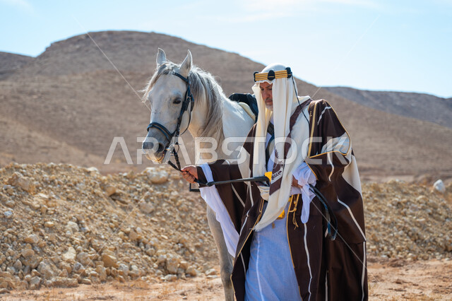 يوم بدينا  22 فبراير، رعاية الخيل والاهتمام به في الصحراء، رجل عربي خليجي سعودي يرتدي العقال الذهبي والبشت يمشي برفقة فرسه الأبيض الأصيل, ارتداء الزي الشعبي في المناسبة الوطنية، ذكرى تأسيس الدولة السعودية الأولى في 1727م, توراث حب وتربية الجياد من الأجداد