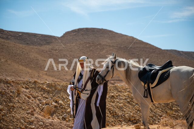 ارتداء الزي الشعبي في المناسبة الوطنية، ذكرى تأسيس الدولة السعودية الأولى في 1727م, توراث حب وتربية الجياد من الأجداد, رعاية الخيل والاهتمام به في الصحراء، رجل عربي خليجي سعودي يرتدي العقال الذهبي والبشت يمشي برفقة فرسه الأبيض الأصيل, يوم بدينا  22 فبراير