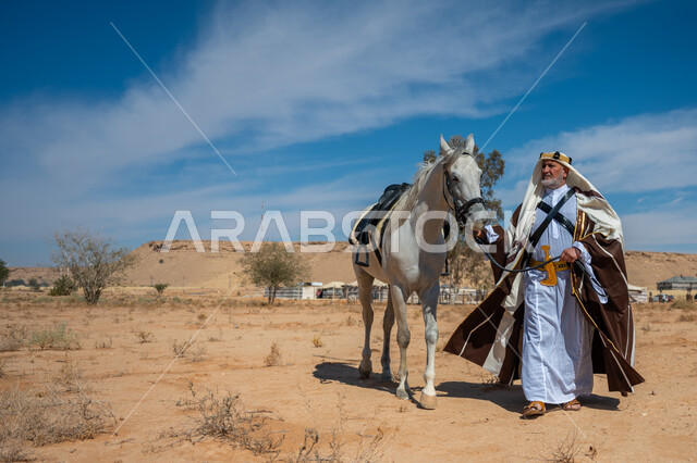 ذكرى تأسيس الدولة السعودية الأولى في 1727م, رعاية الخيل والاهتمام به في الصحراء، رجل عربي خليجي سعودي يرتدي العقال الذهبي والبشت يمشي برفقة فرسه الأبيض الأصيل, ارتداء الزي الشعبي في المناسبة الوطنية، يوم بدينا  22 فبراير، توراث حب وتربية الجياد من الأجداد