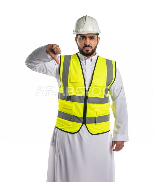 بورتريه لمهندس عربي خليجي سعودي يرتدي الخوذة والسترة الخاصة بالعمل ، يخفض اصبع الابهام لاسفل لعدم اعجابه بشيء ما ،اشراف ومتابعة العمل ،خلفية بيضاء
