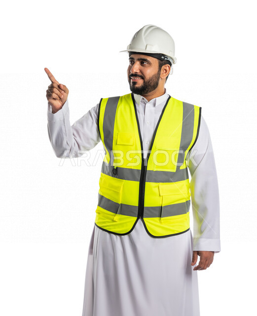 بورتريه لمهندس عربي خليجي سعودي يرتدي الخوذة والسترة الخاصة بالعمل ويشير باصبع السبابة لهدف ما، الاشارة لموقع وبناء، حركة اصبع واشارات، خلفية بيضاء