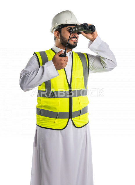 بورتريه لمهندس عربي خليجي سعودي يرتدي خوذة و سترة خاصة بالعمل، يحمل بيده جهاز اتصال لاسلكي، ينظر من خلال المنظار الى مكان ما ، اشراف ومتابعة العمل ،اعطاء اوامر خاصة بالعمل ، مهن و وظائف ، ادارة المشاريع المعمارية الهندسية