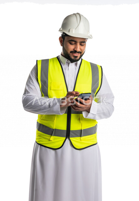 بورتريه لمهندس عربي خليجي سعودي يرتدي الخوذة والسترة الخاصة بالعمل ،يستخدم الهاتف المحمول ،ادارة الاعمال الهندسية عن بعد ، تتبع الاعمال عبر الهاتف المحمول ، مراجعه و تتبع المخططات الهندسية من خلال تطبيق هندسي، خلفية بيضاء