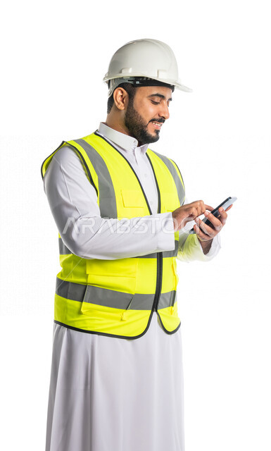 بورتريه لمهندس عربي خليجي سعودي يرتدي الخوذة والسترة الخاصة بالعمل ،يستخدم الهاتف المحمول ،ادارة الاعمال الهندسية عن بعد ، تتبع الاعمال عبر الهاتف المحمول ، مراجعه و تتبع المخططات الهندسية من خلال تطبيق هندسي، خلفية بيضاء