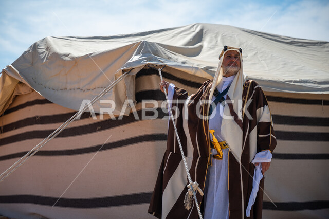 يوم بدينا 22 فبراير، ذكرى تأسيس الدولة السعودية الأولى في 1727م، الشموخ والاعتزاز والفخر، رجل عربي خليجي سعودي يرتدي العقال الذهبي والبشت يقف بجوار الخيمة في الصحراء, ارتداء الزي الشعبي في المناسبة الوطنية، إظهار حب الوطن والانتماء إليه