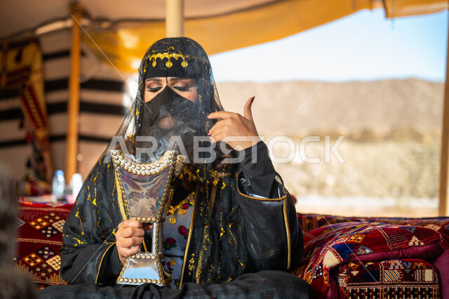 التبخر باستخدام خشب العود والمبخرة العربية بالأعياد والمناسبات الوطنية، ذكرى تأسيس الدوله السعوديه الأولى 1727 م, يوم بدينا 22 فبراير، اتباع عادات وتقاليد المملكة الأصيلة، إمرأة عربية خليجية سعودية ترتدي البرقع و العباءة تقوم بالتعطر والتطيب بالبخور داخل خيمة