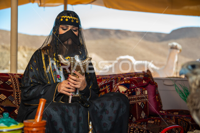 اتباع عادات وتقاليد المملكة الأصيلة، التبخر باستخدام خشب العود والمبخرة العربية بالأعياد والمناسبات الوطنية، ذكرى تأسيس الدوله السعوديه الأولى 1727 م, يوم بدينا 22 فبراير، إمرأة عربية خليجية سعودية ترتدي البرقع و العباءة تقوم بالتعطر والتطيب بالبخور داخل خيمة