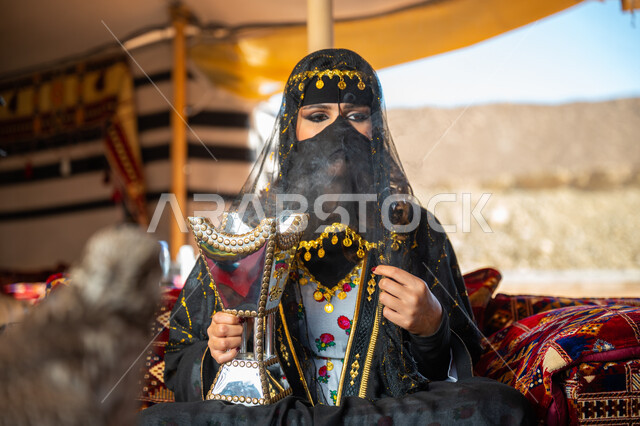 اتباع عادات وتقاليد المملكة الأصيلة، التبخر باستخدام خشب العود والمبخرة العربية بالأعياد والمناسبات الوطنية، ذكرى تأسيس الدوله السعوديه الأولى 1727 م, يوم بدينا 22 فبراير، إمرأة عربية خليجية سعودية ترتدي البرقع و العباءة تقوم بالتعطر والتطيب بالبخور داخل خيمة