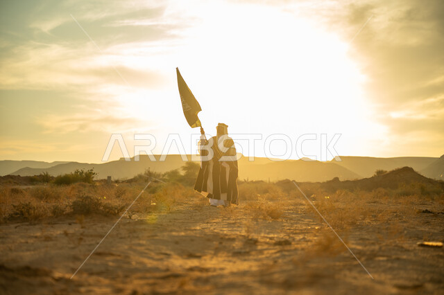 ذكرى تأسيس الدولة السعودية الأولى 1727م, يوم بدينا 22 فبراير, عيد ومناسبة وطنية متميزة, ارتداء زي المنطقة الوسطى, الفخر والاعتزاز بالهوية الوطنية, رجل عربي خليجي سعودي يرتدي البشت والعقال الذهبي يرفع سارية علم المملكة عند شروق الشمس في الصحراء