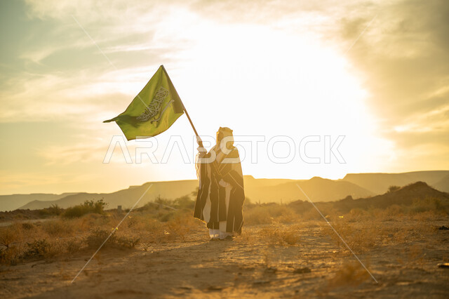 الاحتفال بذكرى تأسيس الدولة السعودية الأولى 1727م, يوم بدينا 22 فبراير, حب الوطن والانتماء اليه, ارتداء زي المنطقة الوسطى, مناسبة وعيد وطني متميز, رجل عربي خليجي سعودي يرتدي البشت والعقال يرفع سارية علم المملكة عند شروق الشمس في الصحراء