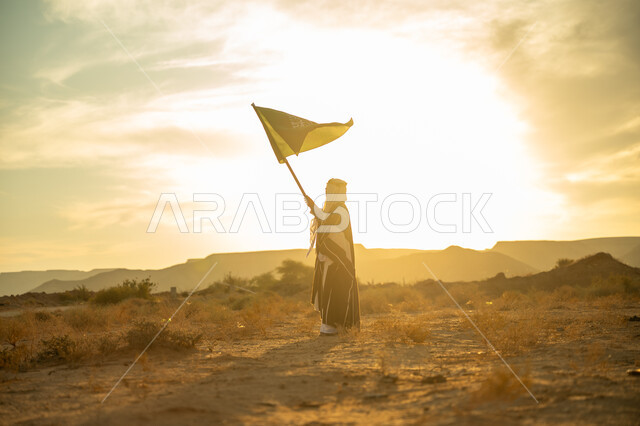 Pride and pride in national identity, wearing the Central Region costume, a special national occasion and holiday, celebrating the anniversary of the founding of the first Saudi state 1727 AD, the day we started on February 22, a Saudi Gulf Arab man wearing a bisht and agal raising the flagpole of the Kingdom at sunrise in the desert