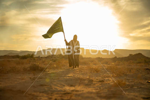 ذكرى تأسيس الدولة السعودية الأولى 1727م, يوم بدينا 22 فبراير, مفهوم حب الوطن والانتماء اليه, ارتداء الزي الشعبي التقليدي في مناسبة وطنية, امرأة عربية خليجي سعودية ترتدي البرقع والعباءة ترفع سارية علم المملكة عند شروق الشمس في الصحراء