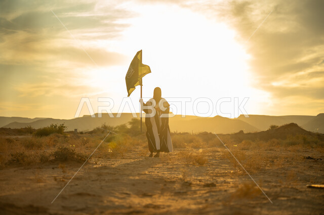الاحتفال بذكرى تأسيس الدولة السعودية الأولى 1727م, يوم بدينا 22 فبراير, مفهوم حب الوطن والانتماء اليه, ارتداء الزي الشعبي التقليدي في مناسبة وطنية, امرأة عربية خليجي سعودية ترتدي البرقع والعباءة ترفع سارية علم المملكة عند شروق الشمس في الصحراء