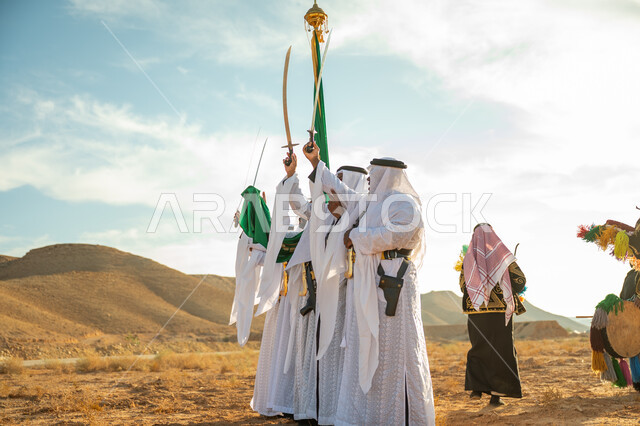 A traditional folklore show in one of the desert areas of the Kingdom, a band celebrating the National Day by dancing with swords and beating drums, the anniversary of the founding of the first Saudi state in 1727 AD, the concept of love of the homeland and belonging to it, the day we started on February 22, wearing the popular Najdi Ardah costume on a national occasion