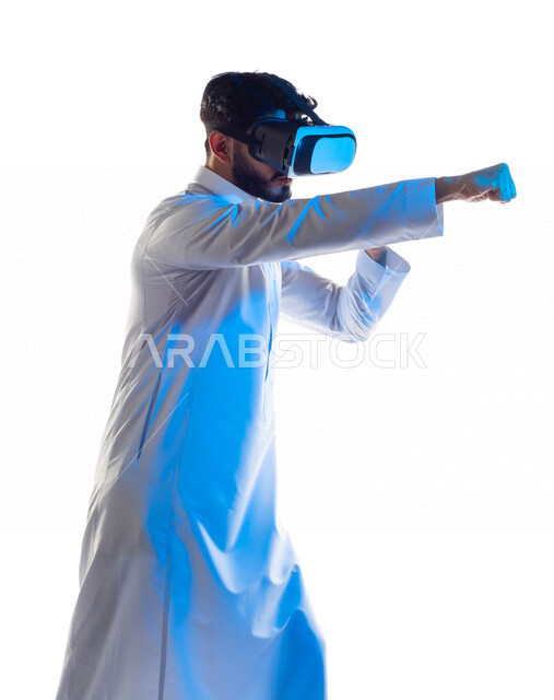 بورتريه لرجل عربي خليجي سعودي يرتدي نظارة الواقع الإفتراضي ثلاثية الأبعاد الفريدة ، يتفاعل بيديه بألعاب الفنون القتالية الدفاعية ، ألعاب العالم الافتراضي ، محاكاة العالم الإفتراضي ، تقنيات و ألعاب ، خلفية بيضاء
