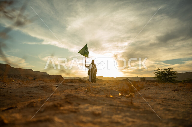 Celebrating the anniversary of the founding of the first Saudi state 1727 AD, wearing traditional folk costume on a national occasion, love of the homeland and belonging to it, the day we started, February 22, a Saudi Arabian Gulf woman wearing a burqa and an abaya raises the flagpole of the Kingdom at sunrise in the desert nature