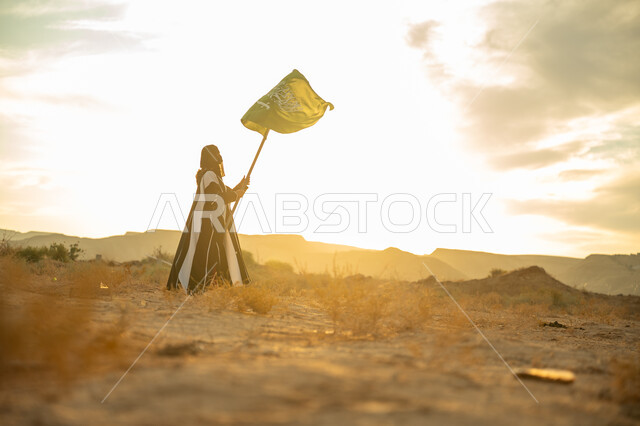 Pride and honor in national identity, the day we started February 22, the anniversary of the founding of the first Saudi state 1727 AD, wearing traditional folk costume on a national occasion, a side view of a Saudi Arabian Gulf woman wearing a burqa and an abaya raising the flagpole of the Kingdom at sunrise in the desert nature