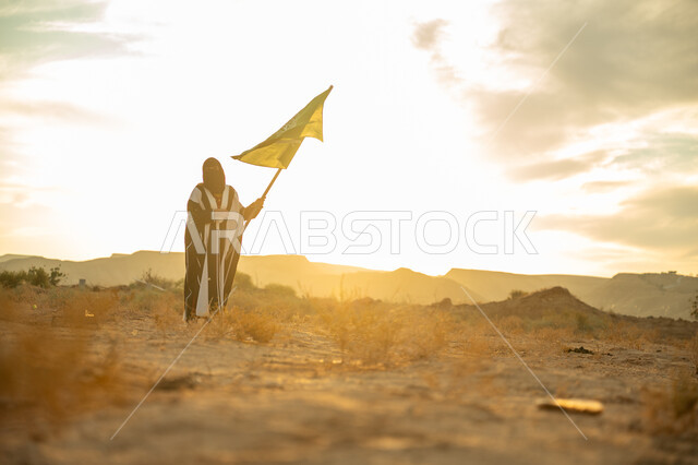 يوم بدينا 22 فبراير, الاحتفال بذكرى تأسيس الدولة السعودية الأولى 1727م, ارتداء الزي الشعبي التقليدي في مناسبة وطنية, مفهوم حب الوطن والانتماء اليه, امرأة عربية خليجي سعودية ترتدي البرقع والعباءة ترفع سارية علم المملكة عند شروق الشمس في الطبيعة الصحراوية