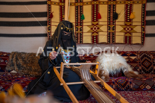 حرفة يدوية تاريخية, منتج محلي وطني، ارتداء الزي الشعبي في المناسبة الوطنية، امرأة عربية خليجية سعودية ترتدي العباءة والبرقع تجلس داخل الخيمة تقوم بحياكة وغزل الأنسجة والقماش, مهنة تقليدية قديمة, يوم بدينا  22 فبراير، ذكرى تأسيس الدولة السعودية الأولى في 1727م