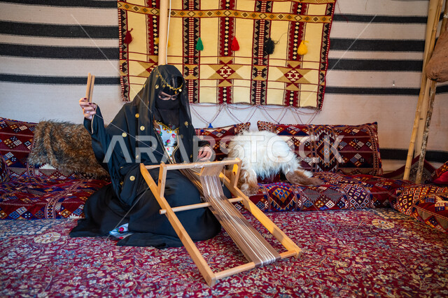حرفة يدوية تاريخية, منتج محلي وطني، ارتداء الزي الشعبي في المناسبة الوطنية، امرأة عربية خليجية سعودية ترتدي العباءة والبرقع تجلس داخل الخيمة تقوم بحياكة وغزل الأنسجة والقماش, مهنة تقليدية قديمة, يوم بدينا  22 فبراير، ذكرى تأسيس الدولة السعودية الأولى في 1727م