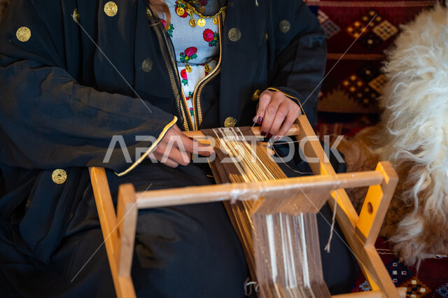 مهنة تقليدية قديمة, ارتداء الزي الشعبي في المناسبة الوطنية، ذكرى تأسيس الدولة السعودية الأولى في 1727م، صورة مقربة لامرأة عربية خليجية سعودية ترتدي العباءة تقوم بحياكة وغزل الأنسجة والقماش, يوم بدينا  22 فبراير، حرفة يدوية تاريخية, منتج محلي وطني