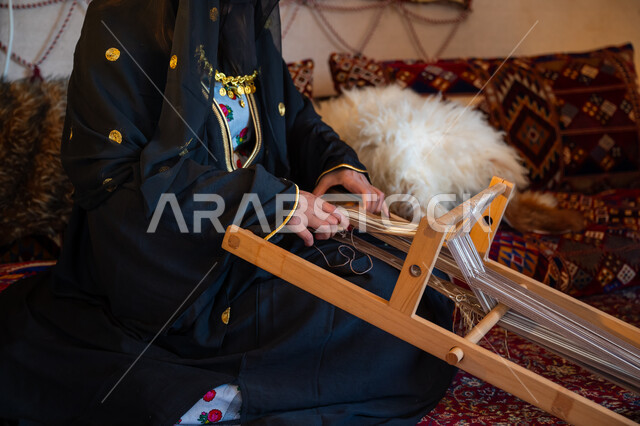 ذكرى تأسيس الدولة السعودية الأولى في 1727م، صورة مقربة لامرأة عربية خليجية سعودية ترتدي العباءة والبرقع تقوم بحياكة وغزل الأنسجة والقماش, مهنة تقليدية قديمة, يوم بدينا  22 فبراير، حرفة يدوية تاريخية, منتج محلي وطني، ارتداء الزي الشعبي في المناسبة الوطنية