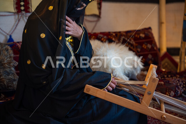 Historical handicraft, national local product, wearing traditional costume on national occasion, close-up of a Saudi Arabian Gulf woman wearing an abaya and burqa, weaving and spinning fabrics and cloth, an ancient traditional profession, the day we started February 22, the anniversary of the founding of the first Saudi state in 1727 AD