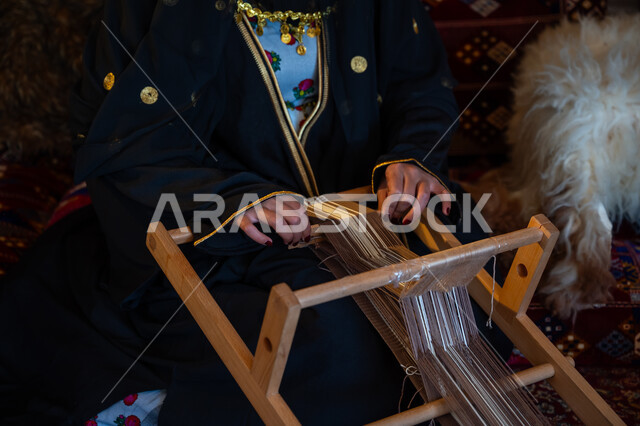 ارتداء الزي الشعبي في المناسبة الوطنية، ذكرى تأسيس الدولة السعودية الأولى في 1727م، صورة مقربة لامرأة عربية خليجية سعودية ترتدي العباءة تقوم بحياكة وغزل الأنسجة والقماش, مهنة تقليدية قديمة, يوم بدينا  22 فبراير، حرفة يدوية تاريخية, منتج محلي وطني