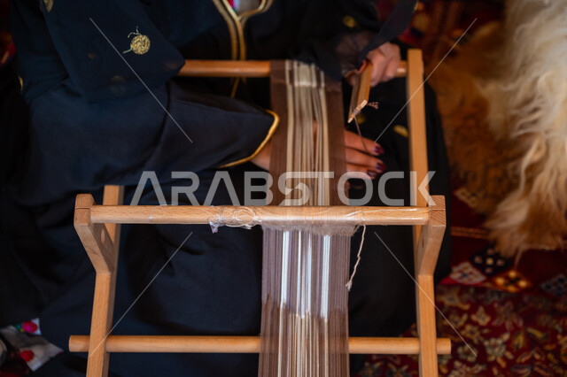 مهنة تقليدية قديمة, ارتداء الزي الشعبي في المناسبة الوطنية، ذكرى تأسيس الدولة السعودية الأولى في 1727م، صورة مقربة لامرأة عربية خليجية سعودية ترتدي العباءة تقوم بحياكة وغزل الأنسجة والقماش, يوم بدينا  22 فبراير، حرفة يدوية تاريخية, منتج محلي وطني