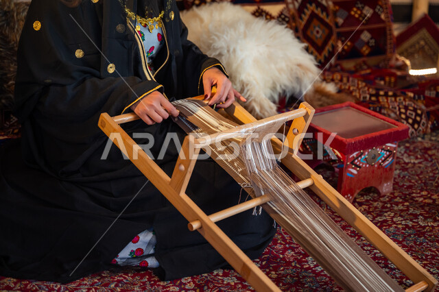 The day we started is February 22, an ancient traditional profession, wearing traditional costume on the national occasion, the anniversary of the founding of the first Saudi state in 1727 AD, a close-up photo of a Saudi Gulf Arab woman wearing an abaya and a burqa, weaving and spinning fabrics and cloth, a historical handicraft, a local national product