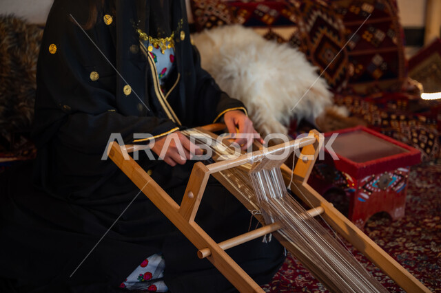 يوم بدينا  22 فبراير، مهنة تقليدية قديمة, ارتداء الزي الشعبي في المناسبة الوطنية، ذكرى تأسيس الدولة السعودية الأولى في 1727م، صورة مقربة لامرأة عربية خليجية سعودية ترتدي العباءة والبرقع تقوم بحياكة وغزل الأنسجة والقماش, حرفة يدوية تاريخية, منتج محلي وطني