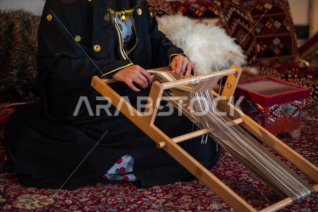 مهنة تقليدية قديمة, ارتداء الزي الشعبي في المناسبة الوطنية، ذكرى تأسيس الدولة السعودية الأولى في 1727م، صورة مقربة لامرأة عربية خليجية سعودية ترتدي العباءة والبرقع تقوم بحياكة وغزل الأنسجة والقماش, يوم بدينا  22 فبراير، حرفة يدوية تاريخية, منتج محلي وطني