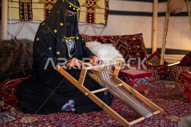 مهنة تقليدية قديمة, يوم بدينا  22 فبراير، ارتداء الزي الشعبي في المناسبة الوطنية، امرأة عربية خليجية سعودية ترتدي العباءة والبرقع تجلس داخل الخيمة تقوم بحياكة وغزل الأنسجة والقماش, حرفة يدوية تاريخية, منتج محلي وطني، ذكرى تأسيس الدولة السعودية الأولى في 1727م