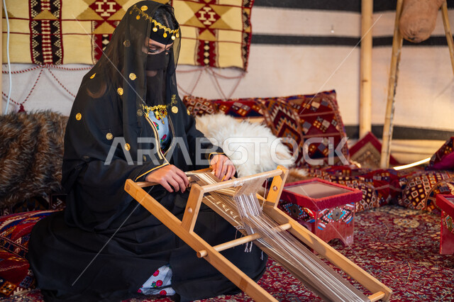 حرفة يدوية تاريخية, مهنة تقليدية قديمة, يوم بدينا  22 فبراير، ارتداء الزي الشعبي في المناسبة الوطنية، امرأة عربية خليجية سعودية ترتدي العباءة والبرقع تجلس داخل الخيمة تقوم بحياكة وغزل الأنسجة والقماش, منتج محلي وطني، ذكرى تأسيس الدولة السعودية الأولى في 1727م