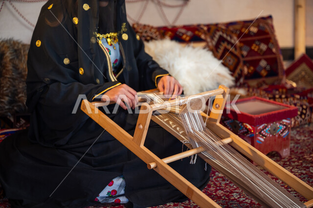 مهنة تقليدية قديمة, ارتداء الزي الشعبي في المناسبة الوطنية، ذكرى تأسيس الدولة السعودية الأولى في 1727م، صورة مقربة لامرأة عربية خليجية سعودية ترتدي العباءة والبرقع تقوم بحياكة وغزل الأنسجة والقماش, يوم بدينا  22 فبراير، حرفة يدوية تاريخية, منتج محلي وطني