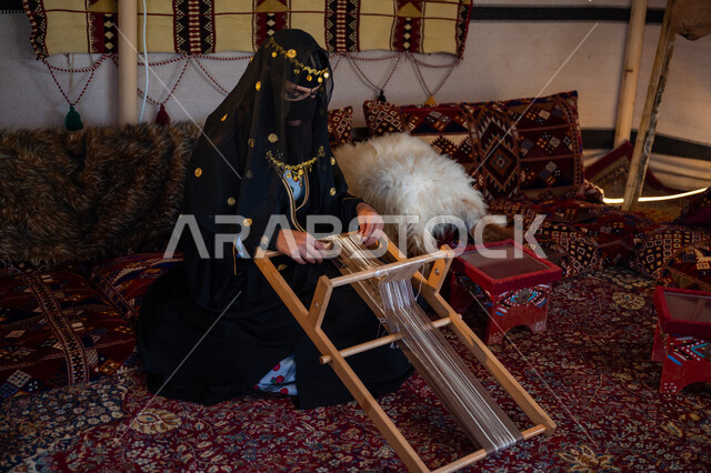 حرفة يدوية تاريخية, مهنة تقليدية قديمة, يوم بدينا  22 فبراير، ارتداء الزي الشعبي في المناسبة الوطنية، امرأة عربية خليجية سعودية ترتدي العباءة والبرقع تجلس داخل الخيمة تقوم بحياكة وغزل الأنسجة والقماش, منتج محلي وطني، ذكرى تأسيس الدولة السعودية الأولى في 1727م