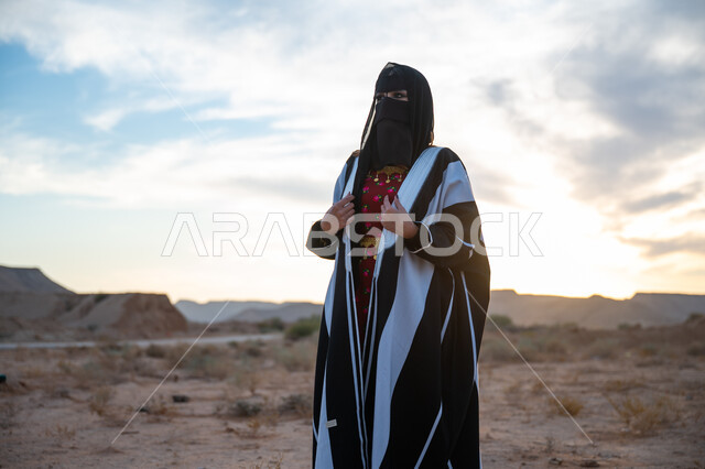 حب الوطن والانتماء اليه, ذكرى تأسيس الدولة السعودية الأولى 1727 م، يوم بدينا 22 فبراير، العناية والاهتمام بالمظهر الخارجي، ارتداء زي المنطقة الوسطى في المناسبة الوطنية، امرأة خليجية عربية سعودية ترتدي العباءة والبرقع الاسود تقف في الطبيعة الصحراوية