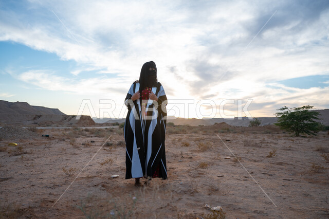 الفخر والاعتزاز بالانتماء للوطن, ذكرى تأسيس الدولة السعودية الأولى 1727 م، يوم بدينا 22 فبراير، العناية والاهتمام بالمظهر الخارجي، ارتداء زي المنطقة الوسطى في المناسبة الوطنية، امرأة خليجية عربية سعودية ترتدي العباءة والبرقع الاسود تقف في الطبيعة الصحراوية