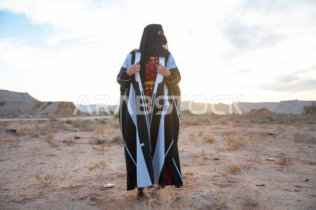 الاهتمام والعناية بالمظهر الخارجي، ارتداء زي المنطقة الوسطى في المناسبة الوطنية، امرأة خليجية عربية سعودية ترتدي العباءة والبرقع الاسود تقف في الطبيعة الصحراوية، يوم بدينا 22 فبراير، ذكرى تأسيس الدولة السعودية الأولى 1727 م، الفخر والاعتزاز بالانتماء للوطن