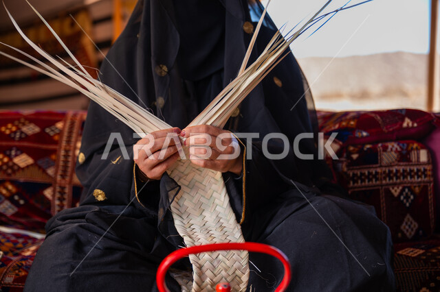 ارتداء الزي الشعبي في المناسبة الوطنية، استخدام أوراق النخيل المجففة في صناعة السلل، حرفة يدوية تقليدية, ذكرى تأسيس الدولة السعودية الأولى في 1727م، صورة مقربة لامرأة عربية خليجية سعودية ترتدي النقاب والعباءة تجلس في خيمة في الصحراء تقوم بجدل سعائف الخوص, يوم بدينا 22 فبراير