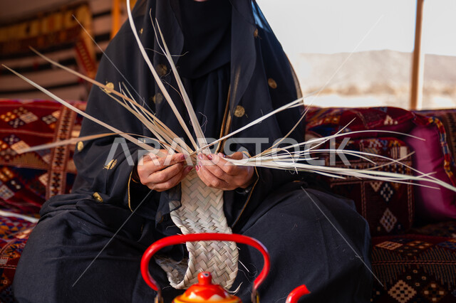 استخدام أوراق النخيل المجففة في صناعة السلل، حرفة يدوية تقليدية, ذكرى تأسيس الدولة السعودية الأولى في 1727م، صورة مقربة لامرأة عربية خليجية سعودية ترتدي النقاب والعباءة تجلس في خيمة في الصحراء تقوم بجدل سعائف الخوص, ارتداء الزي الشعبي في المناسبة الوطنية، يوم بدينا 22 فبراير