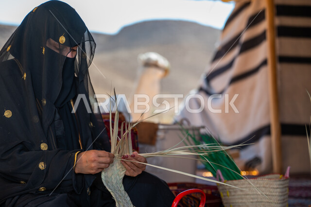 استخدام أوراق النخيل المجففة في صناعة السلل، حرفة يدوية تقليدية, ذكرى تأسيس الدولة السعودية الأولى في 1727م، صورة مقربة لامرأة عربية خليجية سعودية ترتدي النقاب والعباءة تجلس في خيمة في الصحراء تقوم بجدل سعائف الخوص, ارتداء الزي الشعبي في المناسبة الوطنية، يوم بدينا 22 فبراير