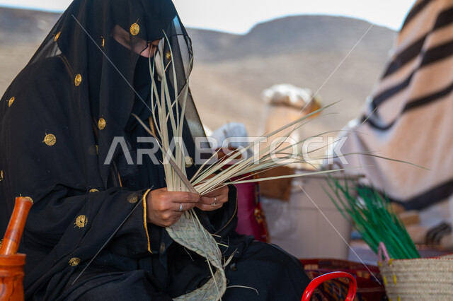ذكرى تأسيس الدولة السعودية الأولى في 1727م، صورة مقربة لامرأة عربية خليجية سعودية ترتدي النقاب والعباءة تجلس في خيمة في الصحراء تقوم بجدل سعائف الخوص, حرفة يدوية تقليدية, يوم بدينا 22 فبراير، ارتداء الزي الشعبي في المناسبة الوطنية، استخدام أوراق النخيل المجففة في صناعة السلل